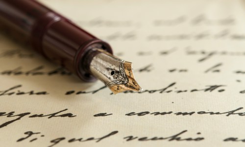 A sheet of paper with black handwriting on which rests the nib and first half of a brown fountain pen