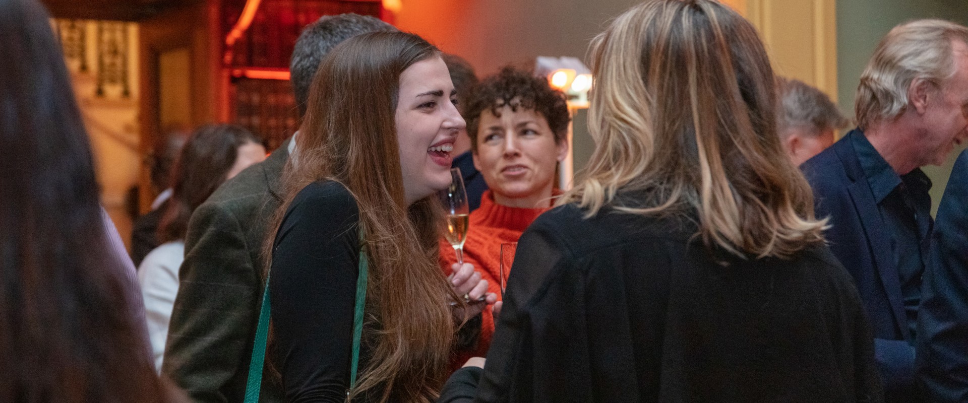 a woman laughing speaking to another person with people around her at an event