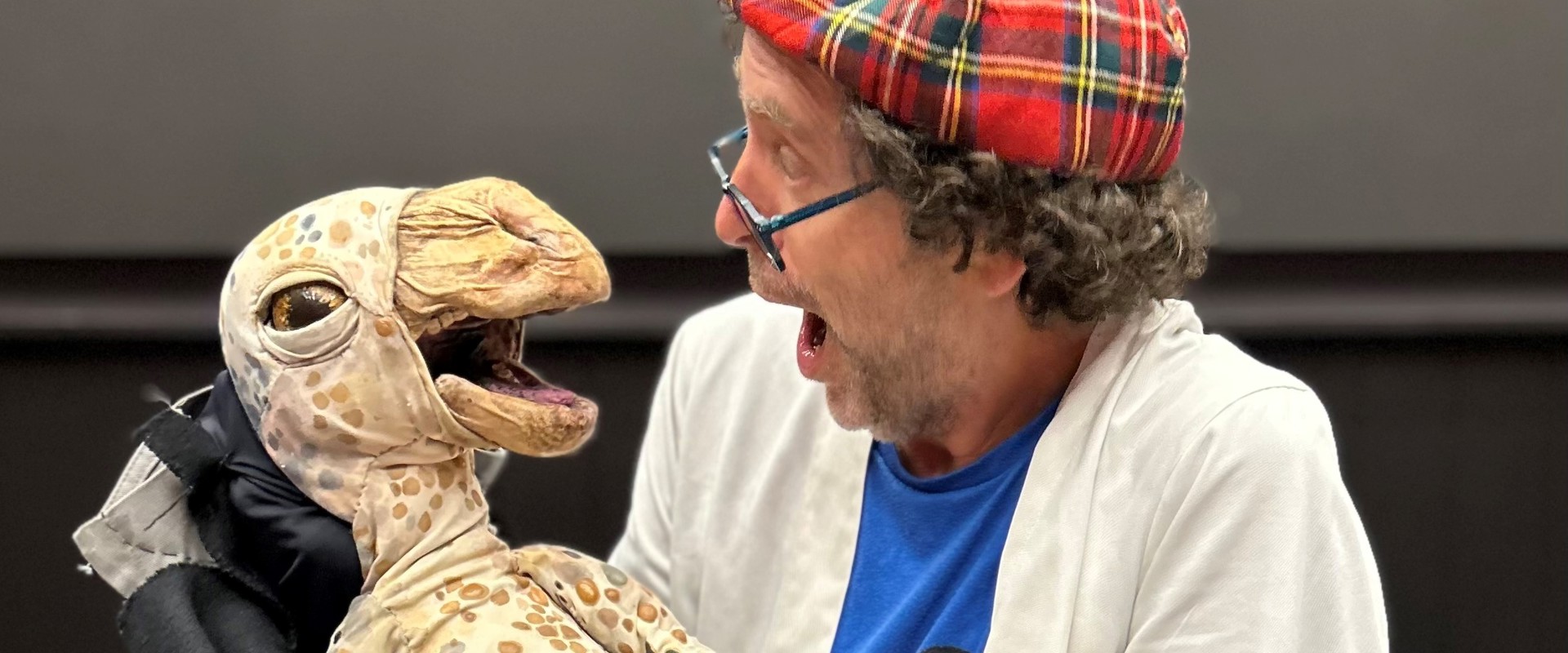 Professor Flint wearing a tartan hat and holding a dinosaur puppet
