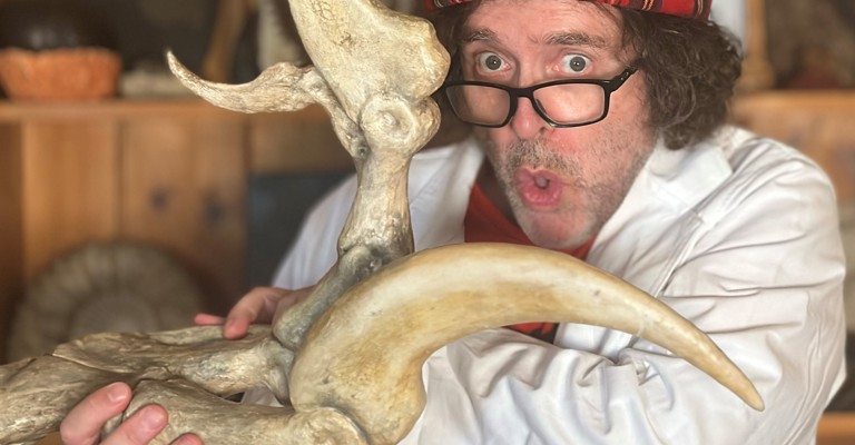 Professor Flint wearing a tartan hat and holding a dinosaur bone