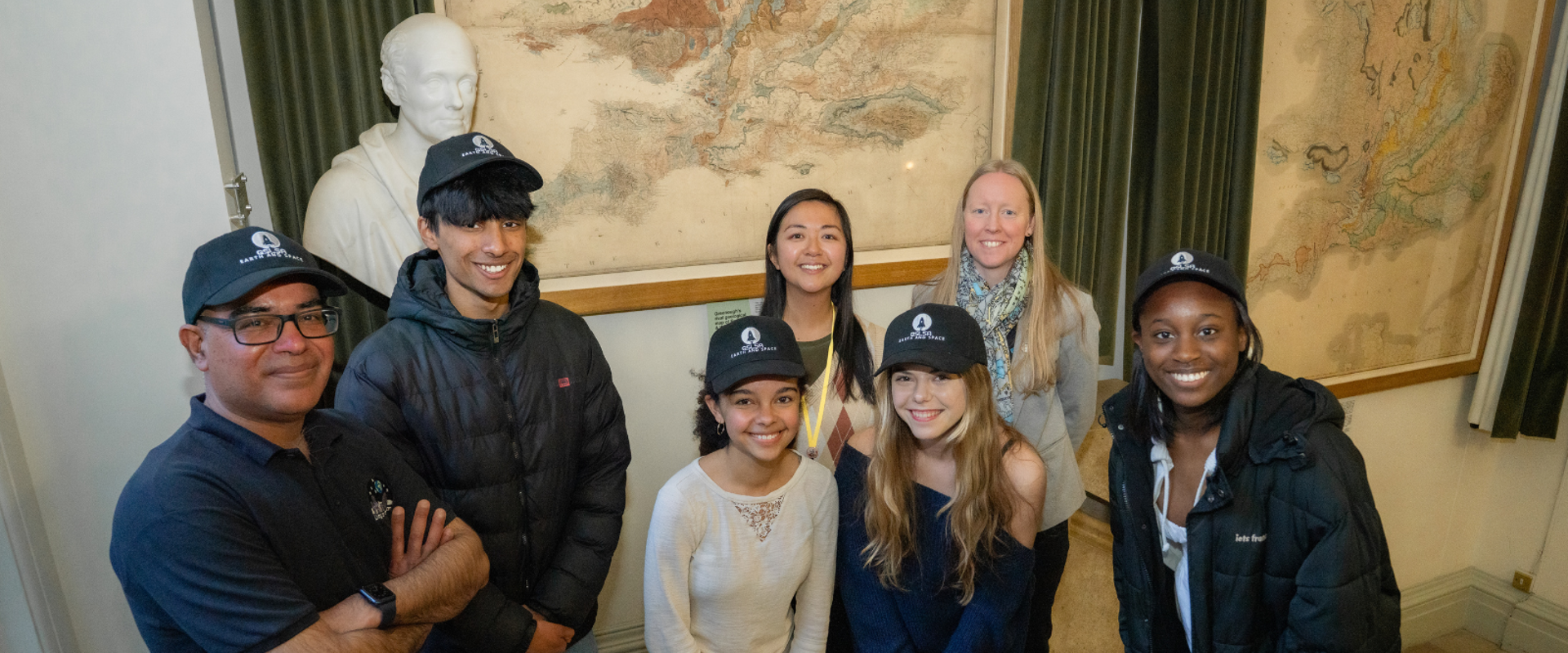 four young people stood with 3 adults smiling at the camera