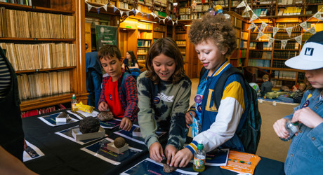 three young boys smiling whilst looking at a display of meteorites on a table
