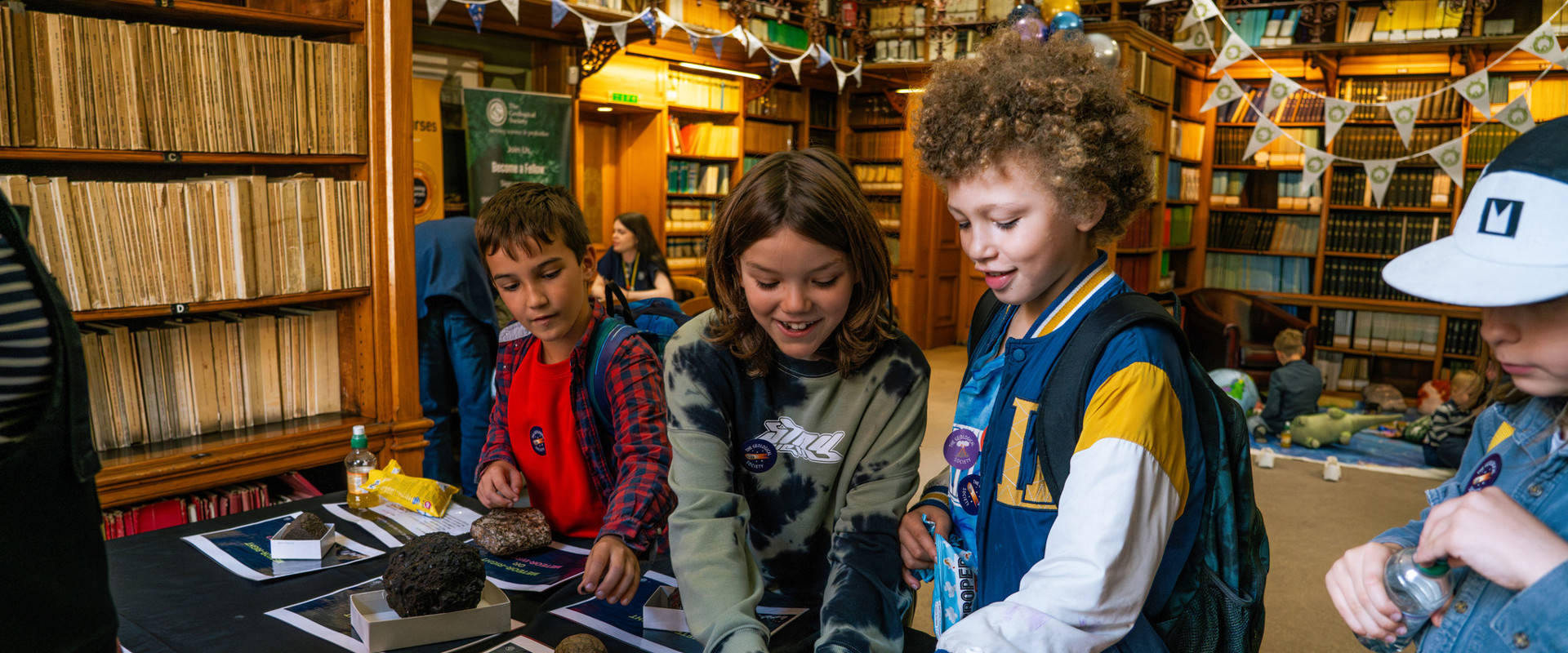 three young boys smiling whilst looking at a display of meteorites on a table