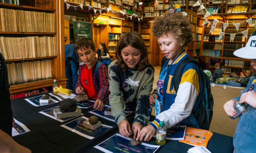 three young boys smiling whilst looking at a display of meteorites on a table