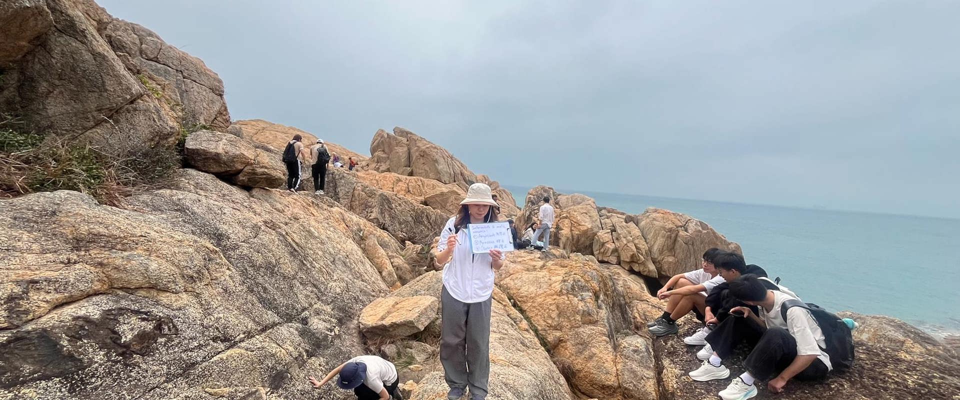 A group of people stand and sit over a rock, studying the geology of the dyke