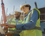 2 people in hardhats on site looking at laptop