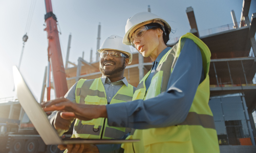 2 people in hardhats on site looking at laptop