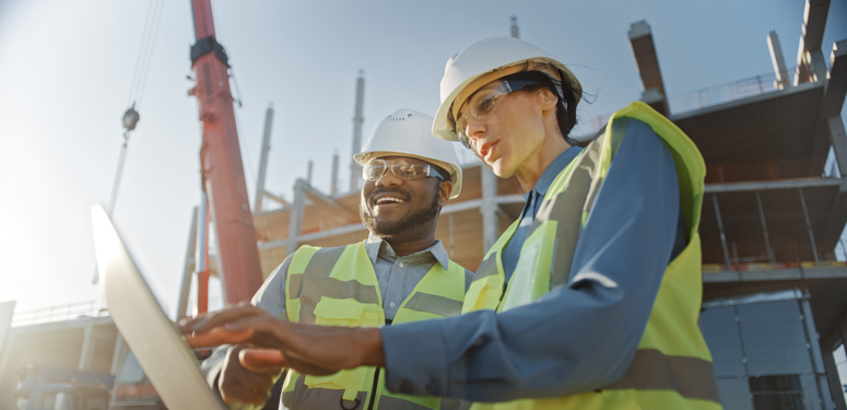 2 people in hardhats on site looking at laptop