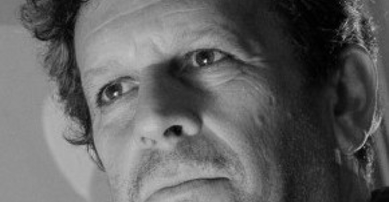 A black and white photo of a man with dark hair looking beyond the camera