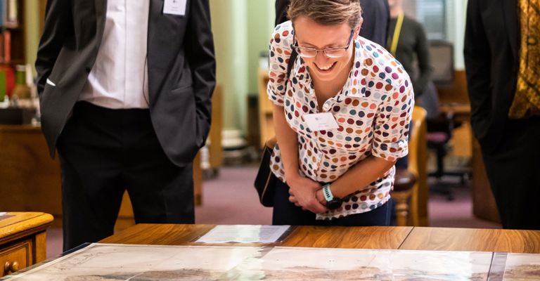In the Geological Society's library, a man and woman look at a geological map on a table, with other men milling in the background