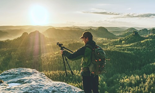 Man on mountaintop holding a camera tripod