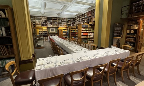 long tables covered in white table cloths and set with glasses and cutlery, within the surroundings of a period library
