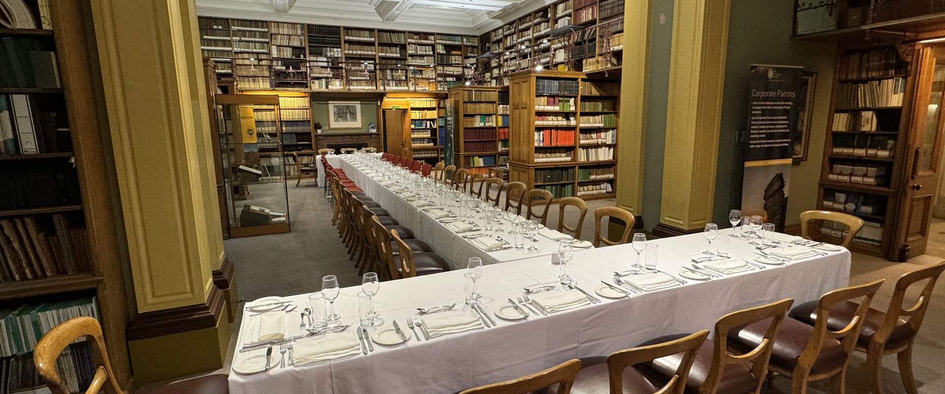 long tables covered in white table cloths and set with glasses and cutlery, within the surroundings of a period library
