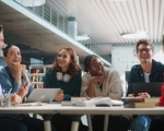 A group of young people around a table with laptops and textbooks laughing