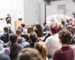 People gathered in lecture hall watching woman give presentation