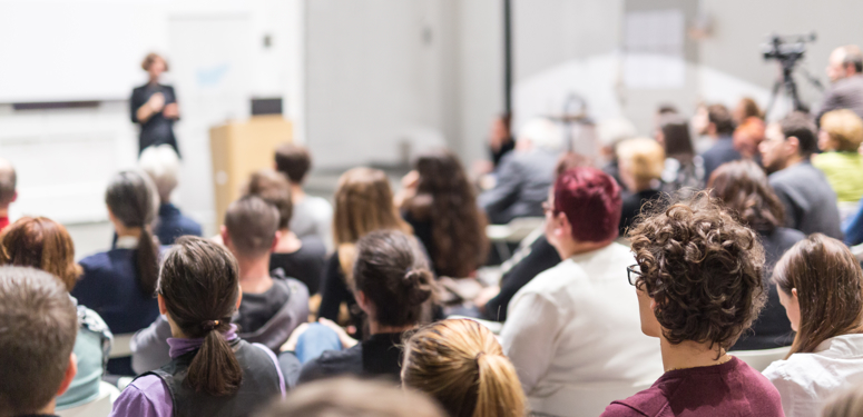 People gathered in lecture hall watching woman give presentation