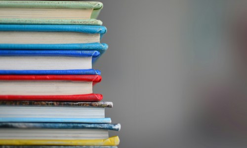 Six books piled one of top of the other, showing coloured edges of spines and covers against a grey background