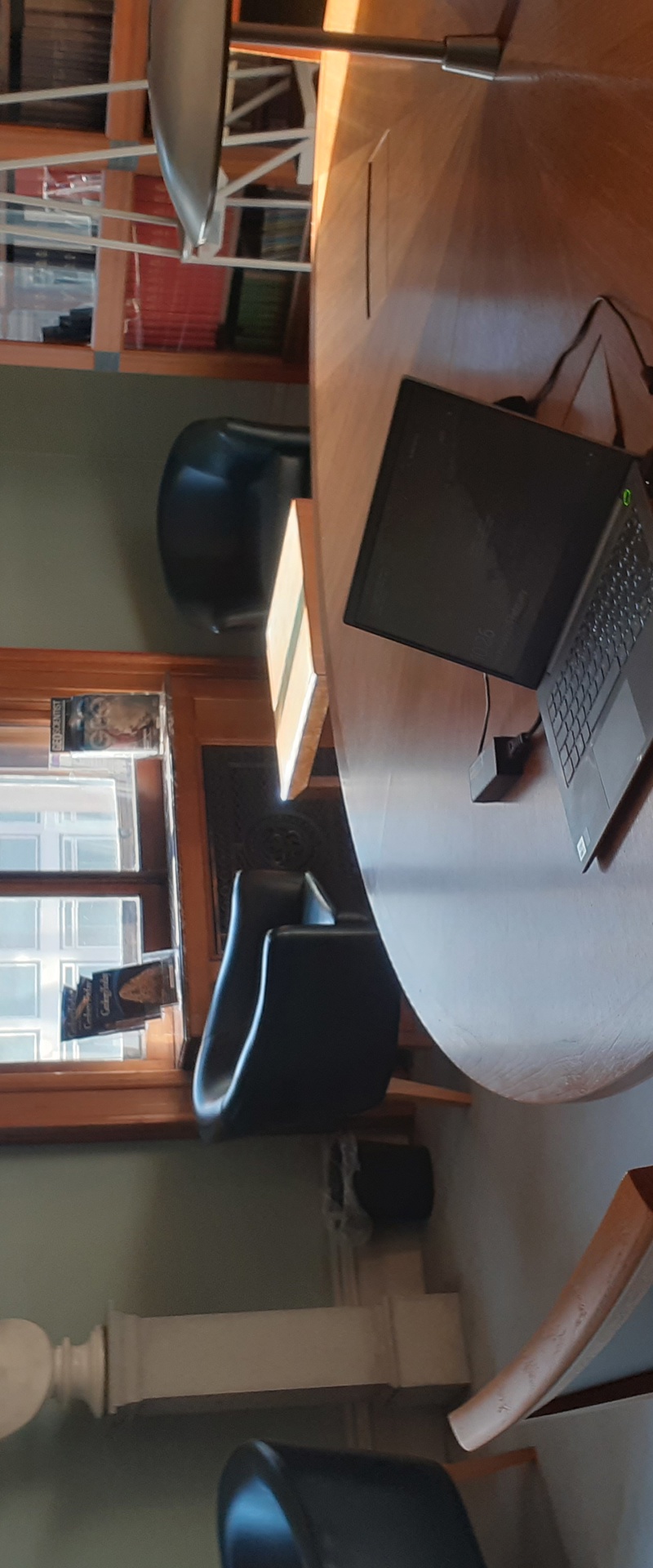 Lyell Room at the Geological Society: a round table with a laptop and chair, in a green painted room with sunlight streaming in.