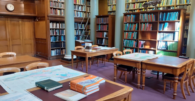 Upper Library of the Geological Society, with books and maps on wooden tables, with sunlight falling on them