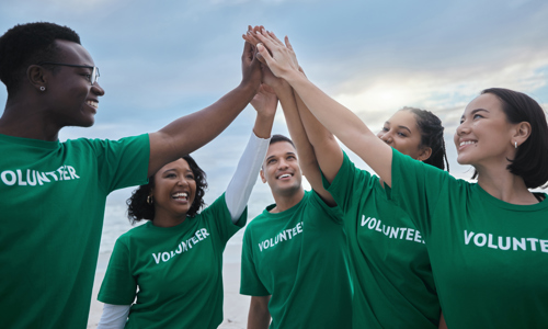 group of five men and women of different ethnicities wearing green t shirts with volunteer written on them, joining their high fives together