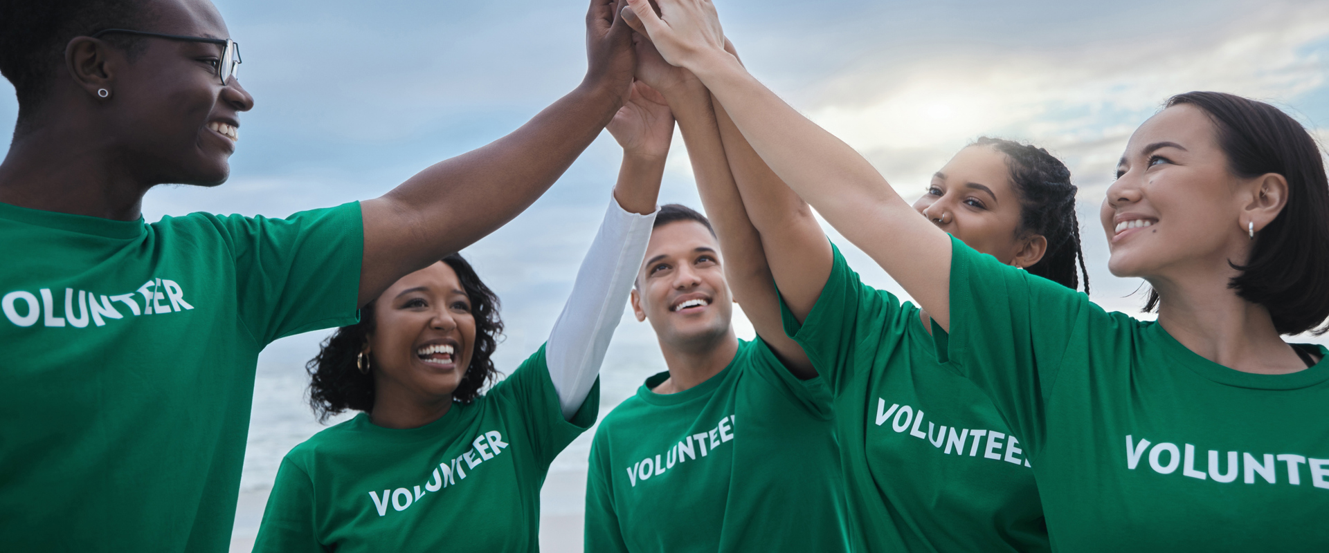 group of five men and women of different ethnicities wearing green t shirts with volunteer written on them, joining their high fives together