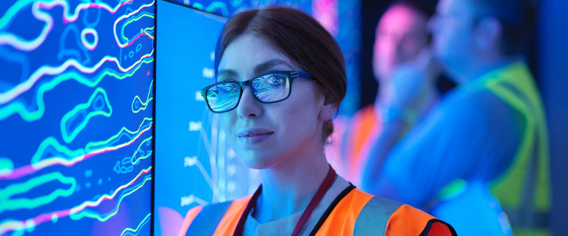 A female geologist in a high-vis vest studying a graphical display board holding an electronic tablet