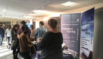 white woman speaking to a black woman at an event stand with postgraduate training on a banner behind them