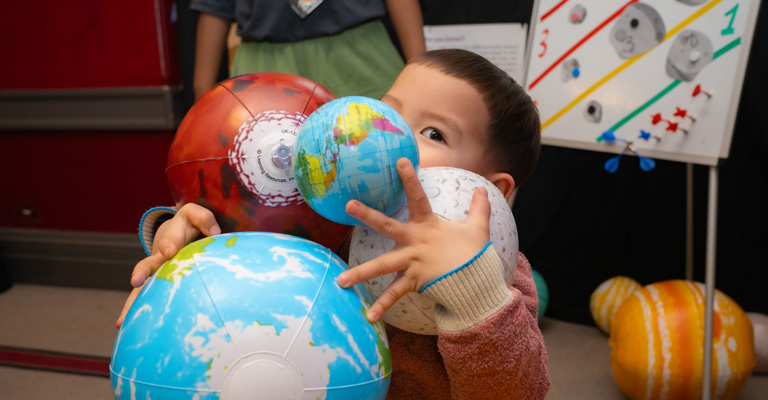 Kid holding inflatable Earths, Moon and planet in an educational, playful setting. 