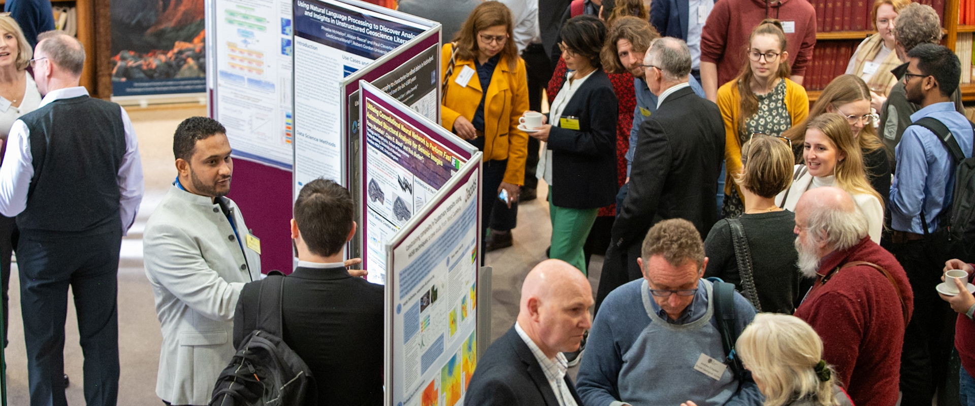 A diverse crowd of individuals in a library, engaged with various informative posters displayed on the walls.