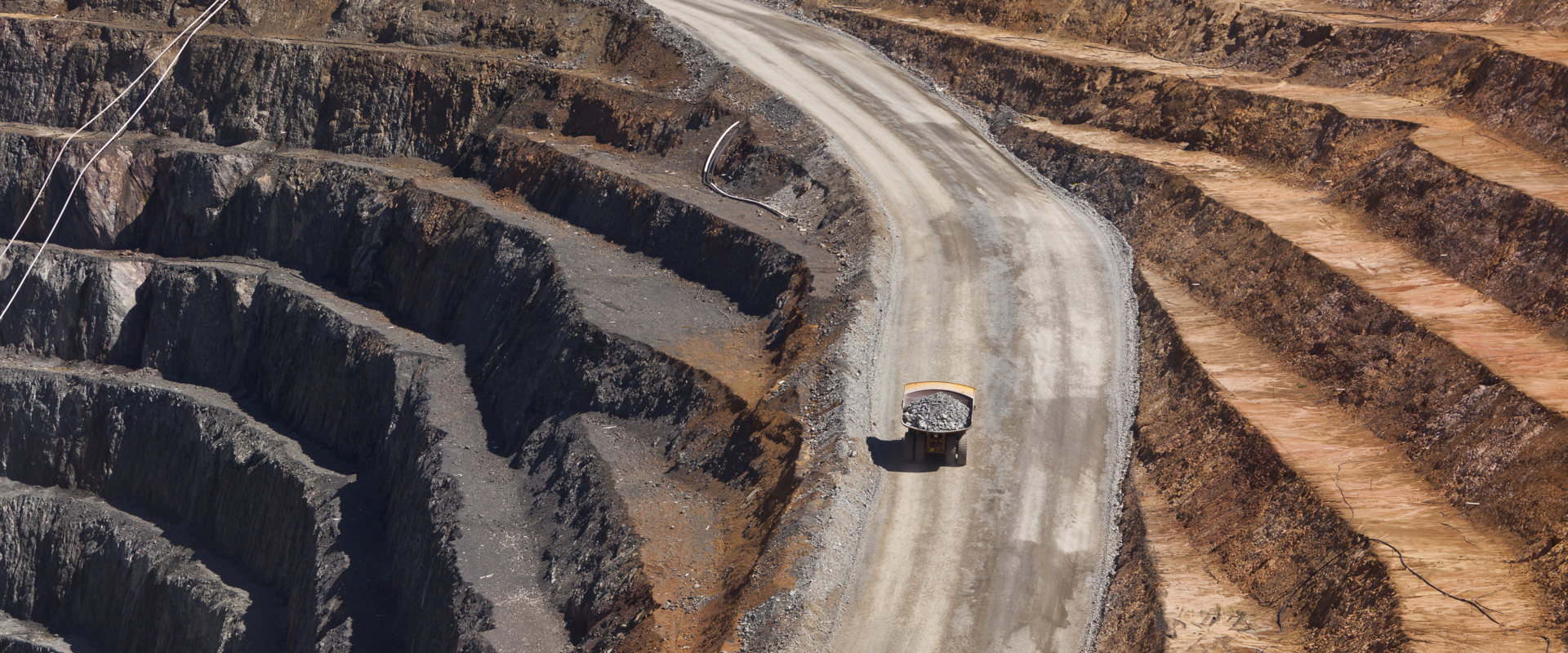 "An open-pit coal mining site with heavy machinery transporting materials along a winding road."