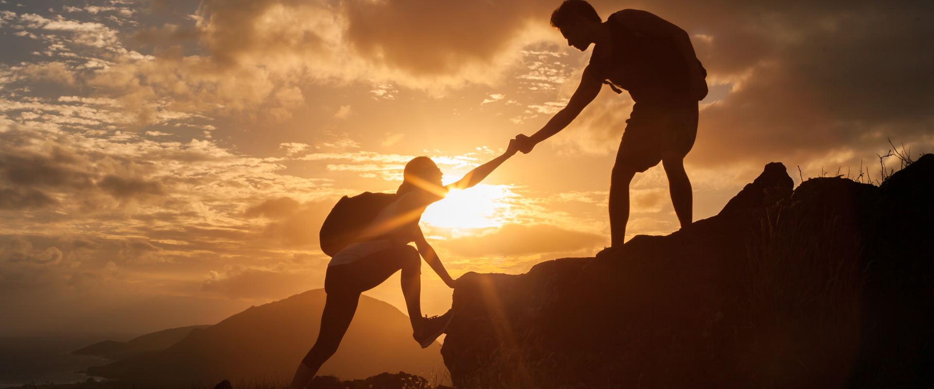 a person reaching out to another person to help them climb up a rocky mountain