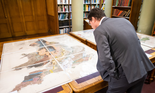 A man in a suit peering over a table with a geological map of England and Wales on it in the Geological Society's Library