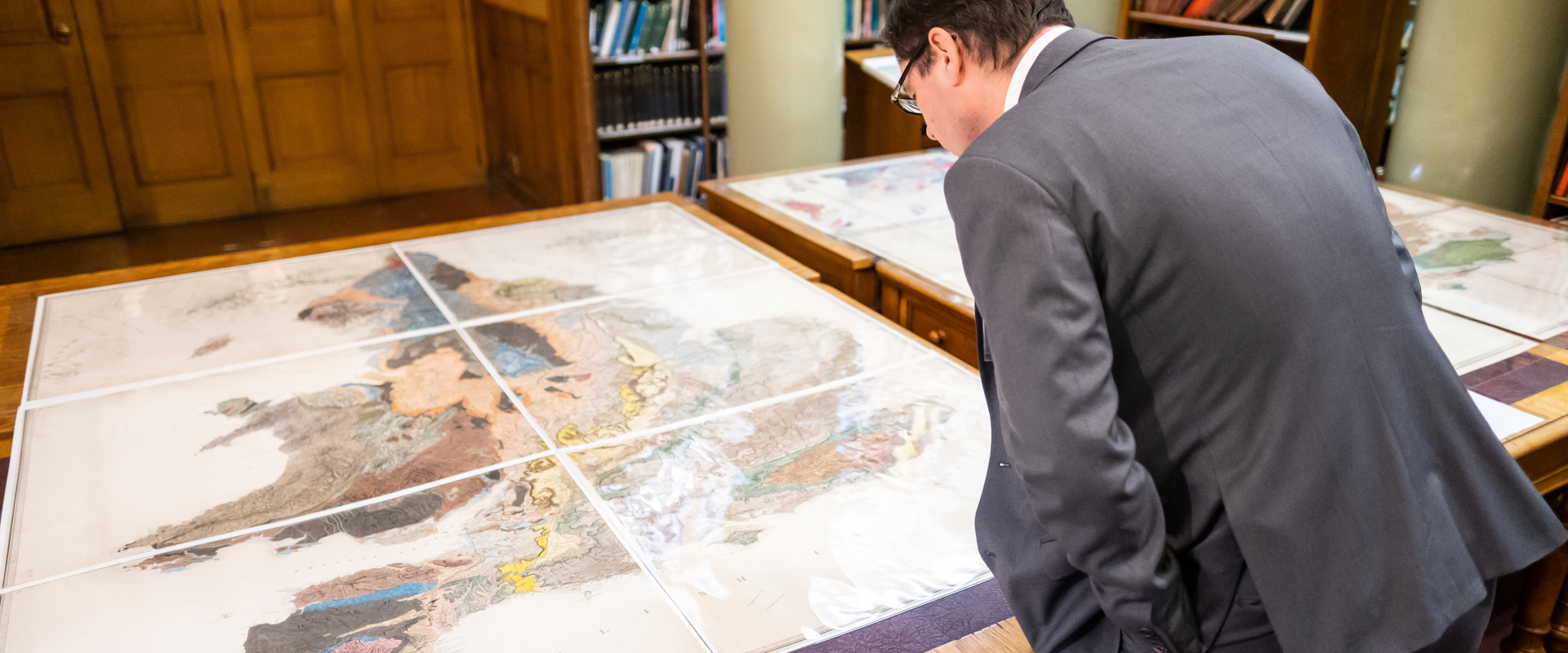 A man in a suit peering over a table with a geological map of England and Wales on it in the Geological Society's Library