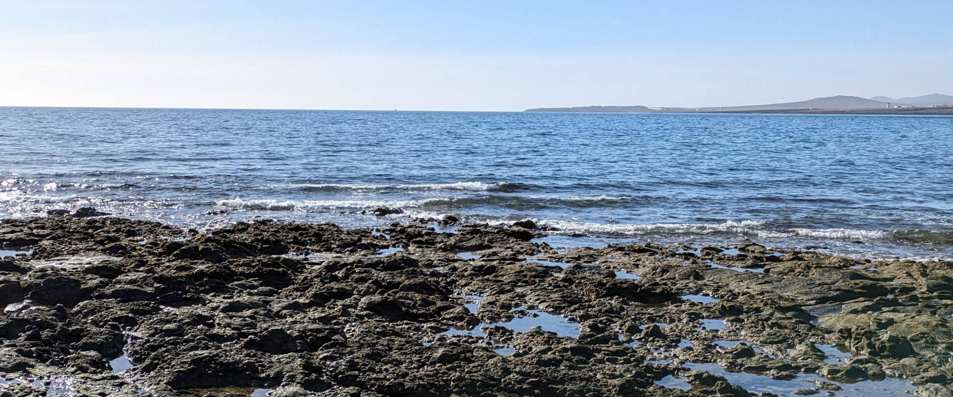Looking out to the sea from a rocky shore, with a blue sky in the background